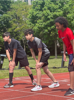 Three boys bend at the knees on a red track.